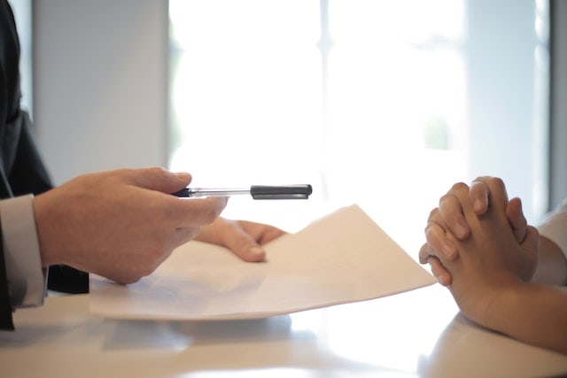 two people exchanging paperwork and a pen for who gets the house in a divorce california
